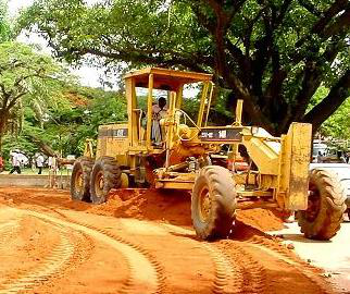 A motor grader leveling and smoothing a dirt road surface