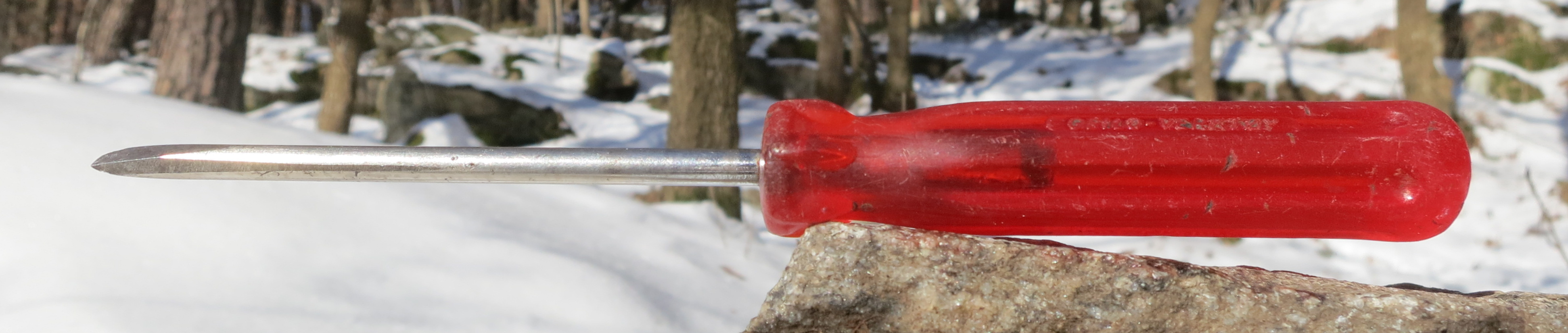 Red-handled screwdriver on a rock outdoors